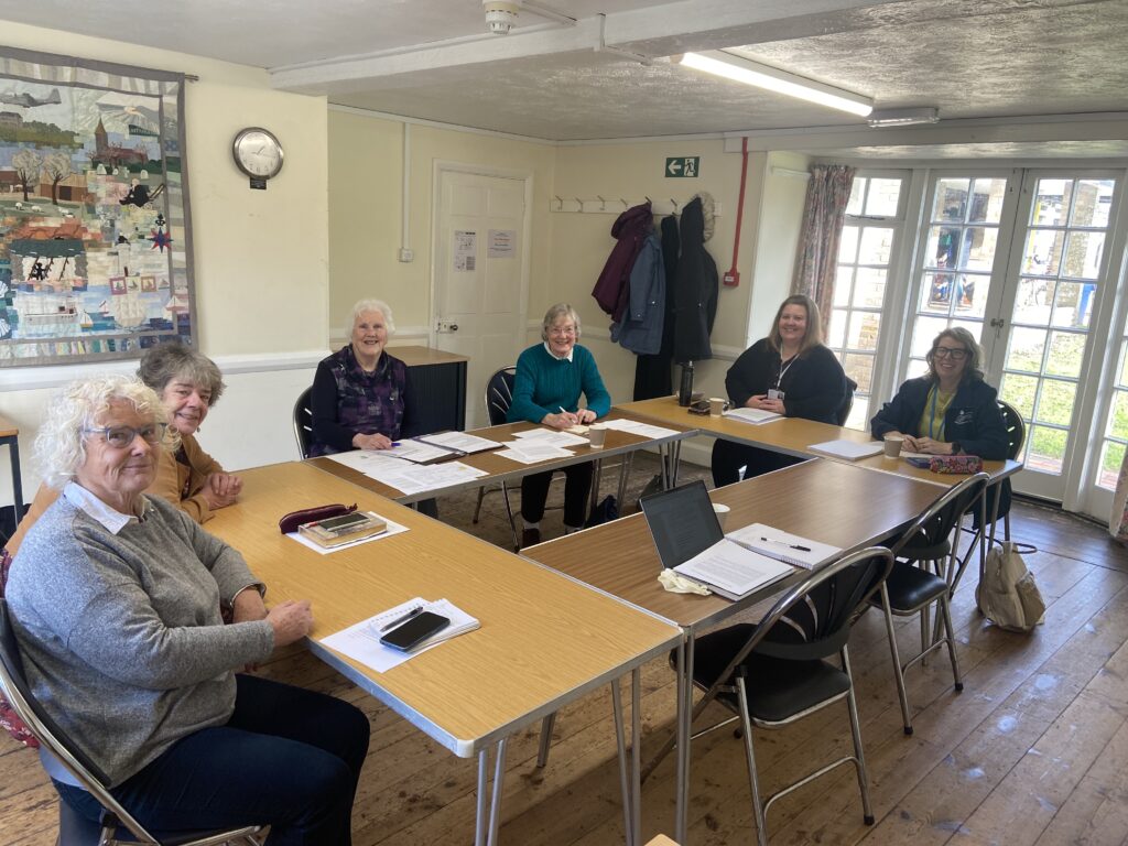 Six people of different ages are sitting at a committee meeting, smiling and looking at the camera.