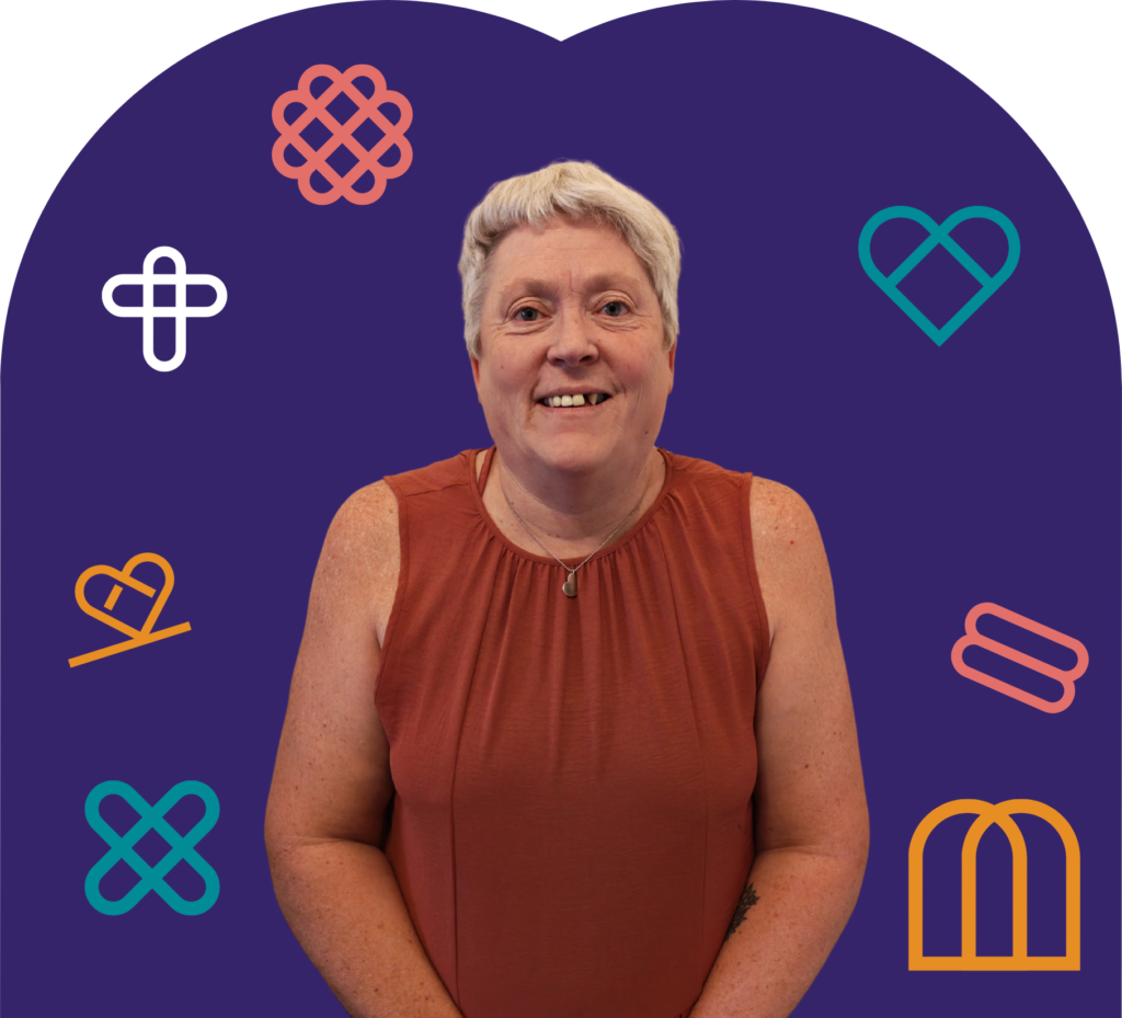 Smiling older woman with short gray hair in an orange sleeveless top, photographed against a dark purple background with colorful abstract logos.